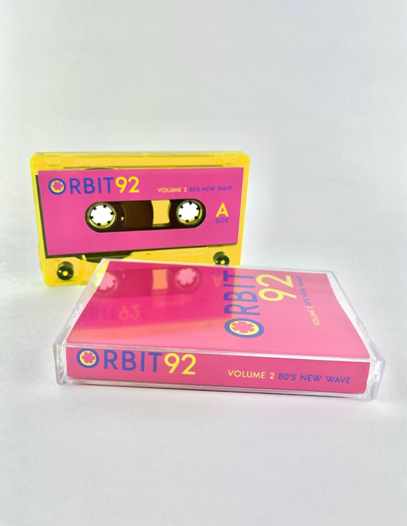 May include: A yellow cassette tape with a pink label. The label says "ORBIT92 VOLUME 2 80'S NEW WAVE".