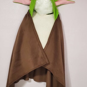 May include: A brown fleece hooded cape with a green hood and pink ears. The hood is shaped like a character from the Star Wars franchise.