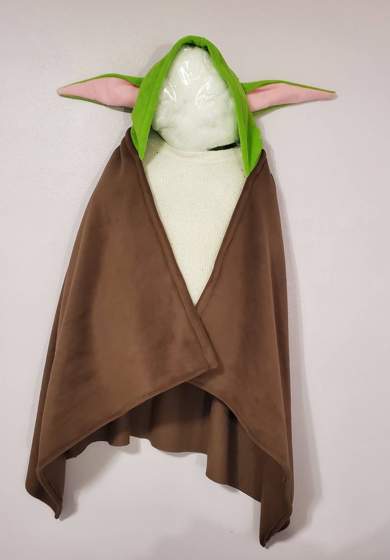 May include: A brown fleece hooded cape with a green hood and pink ears. The hood is shaped like a character from the Star Wars franchise.