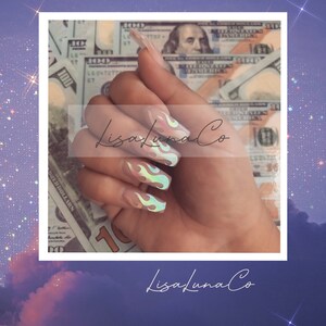Puede incluir: Una mano con uñas largas y transparentes con diseños de llamas iridiscentes. Las uñas están sobre un fondo de billetes de dólar estadounidense. El texto "LisafunaCo" está escrito en la imagen.