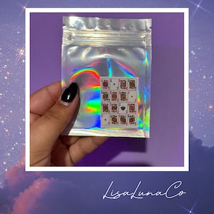May include: A clear plastic bag with a holographic iridescent finish contains a sheet of small playing card stickers. The stickers feature a variety of playing card suits and numbers. The bag has the text "LisaLunaCo" printed on the bottom.