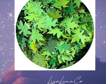 May include: A close-up of a circular container filled with green leaf-shaped glitter. The glitter has a shiny, iridescent finish, reflecting light. The LisaLunaCo logo is at the bottom.