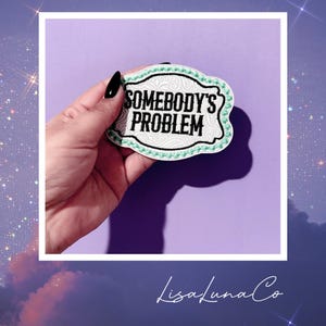 May include: White embroidered patch with a green border and the text "Somebody's Problem" in black lettering.