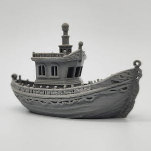 Puede incluir: Un modelo de barco en miniatura gris con detalles intrincados, que incluye una cabina con ventanas y una proa decorativa. El modelo tiene un mástil y un casco detallado, evocando una estética vintage o de fantasía. El barco está sobre un fondo liso.