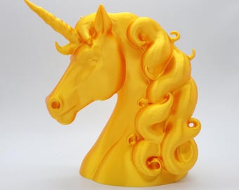 May include: A golden-yellow unicorn head sculpture. The sculpture features a detailed mane, a spiraled horn, and a smooth finish. The unicorn's head is angled slightly to the left, showcasing its profile. The sculpture is a decorative item.