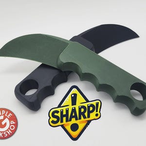 May include: Two curved knives, one dark green and one black, are displayed. The knives have a handle with finger grooves and a curved blade. A yellow and black sign with the word "SHARP!" is visible.