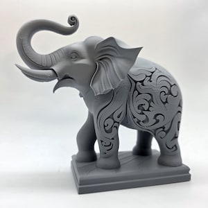 May include: A gray elephant figurine with intricate carved patterns on its body. The elephant has a raised trunk and is standing on a rectangular base. The figurine is a decorative item.