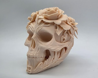 May include: A light peach-coloured skull sculpture with intricate floral detailing. The skull features a crown of roses and detailed carvings around the eye sockets and jawline. A unique decorative piece.