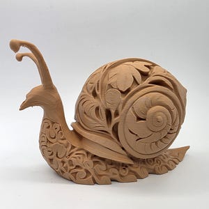 May include: A detailed, brown snail sculpture with an ornate, carved shell featuring leaf and swirl designs. The snail's body and head are also intricately carved, showcasing a unique decorative piece.
