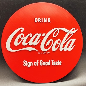 May include: A round, red Coca-Cola sign with white lettering. The sign reads "DRINK Coca-Cola" and "Sign of Good Taste". The classic logo is prominently displayed, making it a recognizable piece of vintage advertising.
