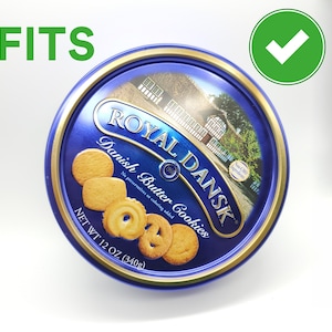 May include: A round blue tin of Royal Dansk Danish Butter Cookies. The tin has a gold rim and features an image of a building and several cookies. The text "Royal Dansk Danish Butter Cookies" is displayed on the tin. The net weight is 12 oz (340g).