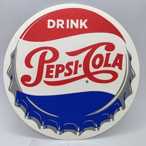 May include: Round Pepsi-Cola sign in a bottle cap design. The sign features a red top section with the word "DRINK" in white, a white center with the Pepsi-Cola logo in red, and a blue bottom section. The edge is silver.