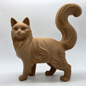May include: A tan-colored cat figurine with detailed fur texture and a curled tail. The cat is standing, with its head turned slightly to the side. The figurine has a smooth finish and is set against a plain white background.