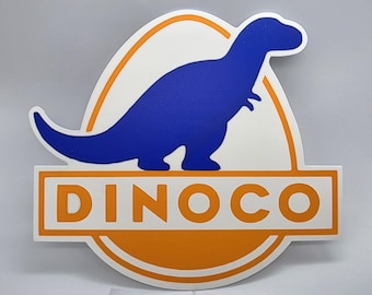 May include: A white and orange Dinoco logo featuring a blue Tyrannosaurus Rex silhouette. The word "DINOCO" is displayed in orange block letters at the bottom of the logo. The logo is set against a light gray background.