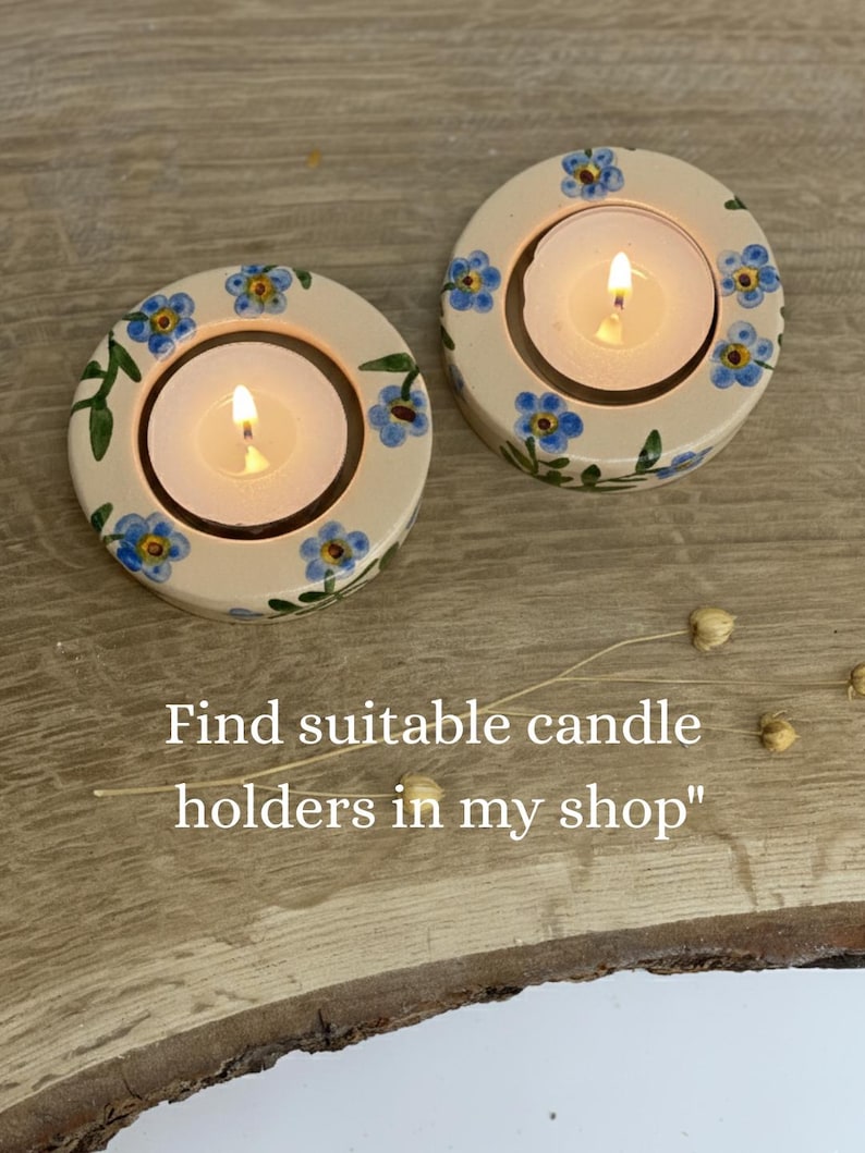 May include: Two cream-colored candle holders with blue floral designs and lit candles. The candle holders have a circular shape with a central opening for the candle. The text "Find suitable candle holders in my shop" is visible.