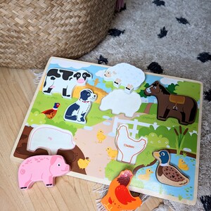 Peut inclure: Un puzzle en bois repr&eacute;sentant des animaux de la ferme : vache, mouton, chien, cheval, cochon, poulet et canard. Les pi&egrave;ces color&eacute;es s'ins&egrave;rent dans les espaces correspondants du plateau. Le mot "Chicken" est imprim&eacute; sur le puzzle.
