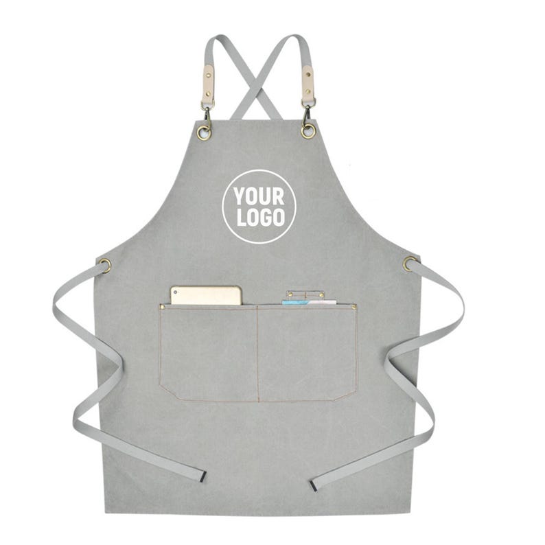 May include: Gray apron with a pocket and leather straps. The apron has a white circle with the text "YOUR LOGO" printed on it. The apron has a pocket with a phone and a notepad inside.