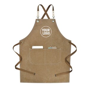 May include: A brown canvas apron with a white pocket and the text "YOUR LOGO" in a white circle. The apron has brown straps and a pocket containing a phone and a small notebook. The apron is designed for use in a kitchen or workshop.
