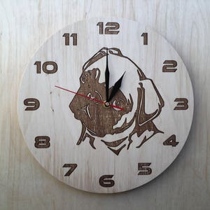 Könnte beinhalten: Eine Holzuhr mit einer braunen Hundesilhouette in der Mitte. Das Zifferblatt der Uhr hat schwarze Zeiger und schwarze Zahlen von 1 bis 12.