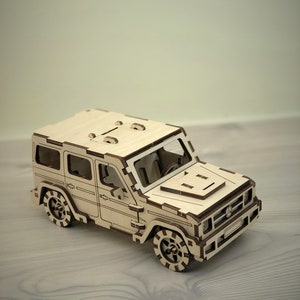 K&ouml;nnte beinhalten: Ein Holzmodell eines hellbraunen SUV mit detailliertem Innenraum und Au&szlig;enbereich. Das Modell hat einen schwarzen K&uuml;hlergrill und schwarze R&auml;der mit einem Reifenprofil.