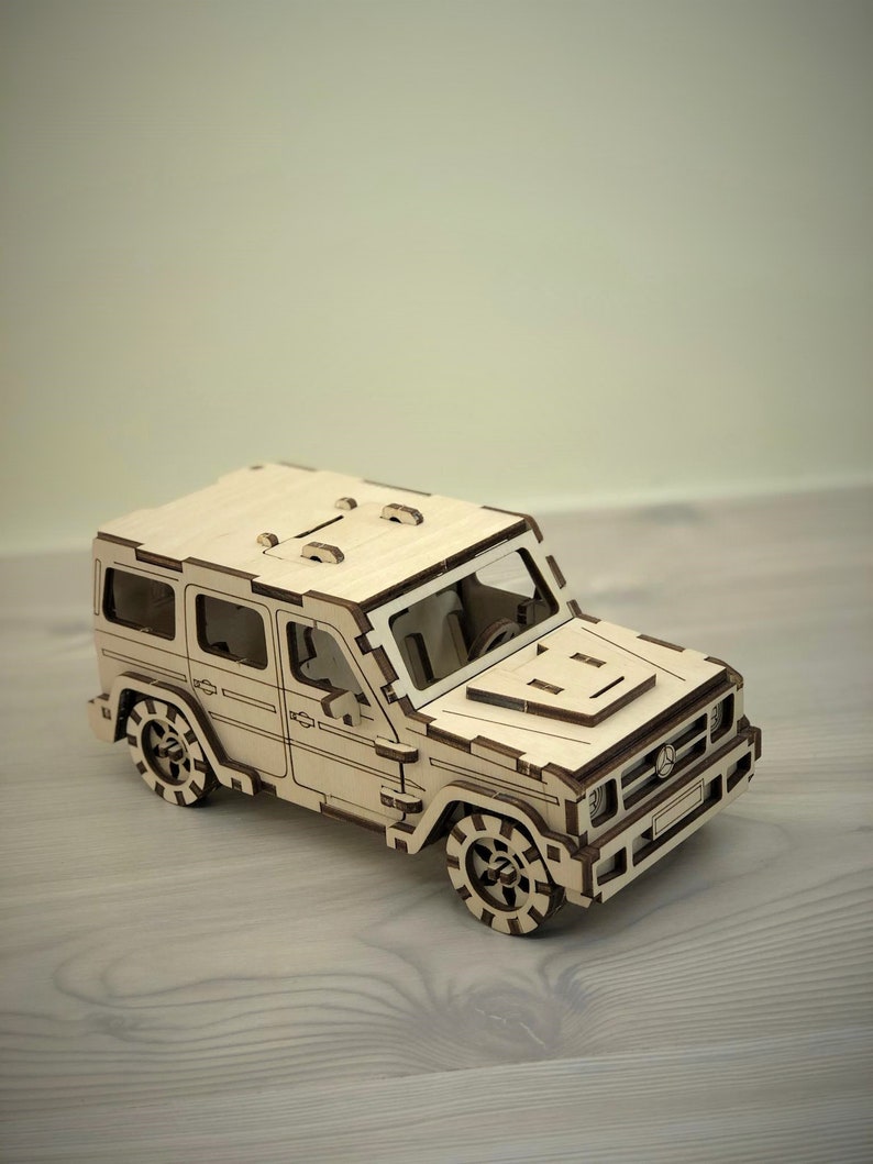 K&ouml;nnte beinhalten: Ein Holzmodell eines hellbraunen SUV mit detailliertem Innenraum und Au&szlig;enbereich. Das Modell hat einen schwarzen K&uuml;hlergrill und schwarze R&auml;der mit einem Reifenprofil.