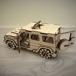 K&ouml;nnte beinhalten: Ein Holzmodell eines viert&uuml;rigen SUVs mit offenem Dach und offener Heckklappe. Das Modell ist aus hellbraunem Holz gefertigt und hat schwarze R&auml;der.