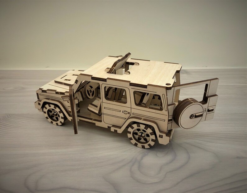 K&ouml;nnte beinhalten: Ein Holzmodell eines viert&uuml;rigen SUVs mit offenem Dach und offener Heckklappe. Das Modell ist aus hellbraunem Holz gefertigt und hat schwarze R&auml;der.