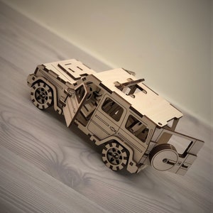 K&ouml;nnte beinhalten: Ein Holzmodell eines Jeeps mit offener T&uuml;r und einem Reserverad am Heck. Das Modell ist aus hellbraunem Holz gefertigt und hat einen detaillierten Innenraum.