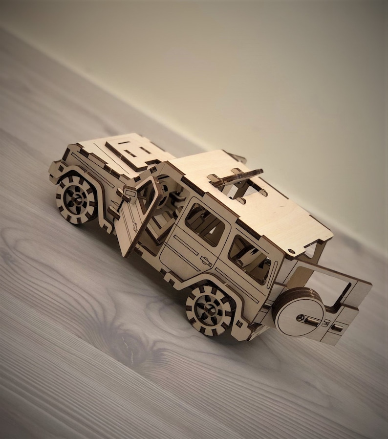 K&ouml;nnte beinhalten: Ein Holzmodell eines Jeeps mit offener T&uuml;r und einem Reserverad am Heck. Das Modell ist aus hellbraunem Holz gefertigt und hat einen detaillierten Innenraum.