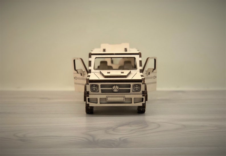 K&ouml;nnte beinhalten: Ein Holzmodell eines Mercedes-Benz G-Wagens mit ge&ouml;ffneten T&uuml;ren. Das Modell ist aus hellem braunem Holz gefertigt und verf&uuml;gt &uuml;ber einen detaillierten Innenraum.