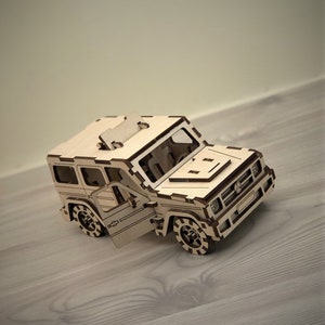 K&ouml;nnte beinhalten: Ein Holzmodell eines Autos mit offener T&uuml;r. Das Modell ist aus hellbraunem Holz gefertigt und hat ein detailliertes Design. Das Auto hat einen schwarzen K&uuml;hlergrill und Scheinwerfer.