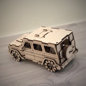 K&ouml;nnte beinhalten: Ein Holzmodell eines viert&uuml;rigen SUVs mit einem Reserverad am Heck. Das Modell ist aus hellem braunem Holz gefertigt und hat ein detailliertes Design.