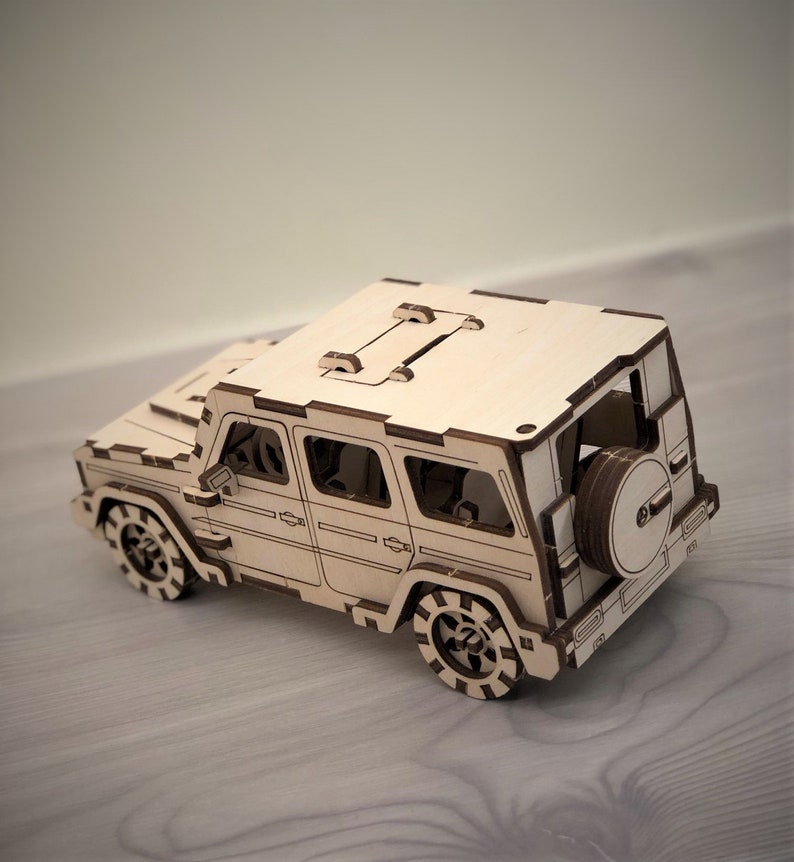 K&ouml;nnte beinhalten: Ein Holzmodell eines viert&uuml;rigen SUVs mit einem Reserverad am Heck. Das Modell ist aus hellem braunem Holz gefertigt und hat ein detailliertes Design.
