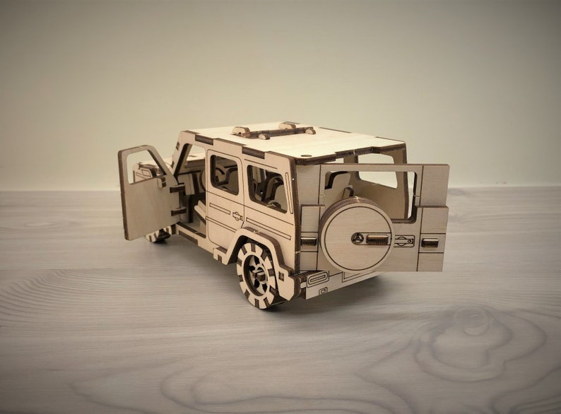 K&ouml;nnte beinhalten: Ein Holzmodell eines hellbraunen SUV mit ge&ouml;ffneten T&uuml;ren. Das Modell hat ein Reserverad hinten und einen detaillierten Innenraum.