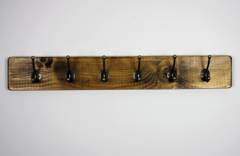 Puede incluir: Un perchero de madera r&uacute;stico con seis ganchos de lat&oacute;n antiguo. El perchero est&aacute; te&ntilde;ido de un color marr&oacute;n oscuro y tiene una veta de madera natural.