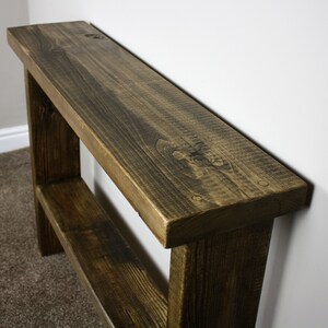May include: A rustic wooden console table with a dark brown stain. The table has a single shelf and is made of reclaimed wood.