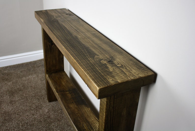 May include: A rustic wooden console table with a dark brown stain. The table has a single shelf and is made of reclaimed wood.