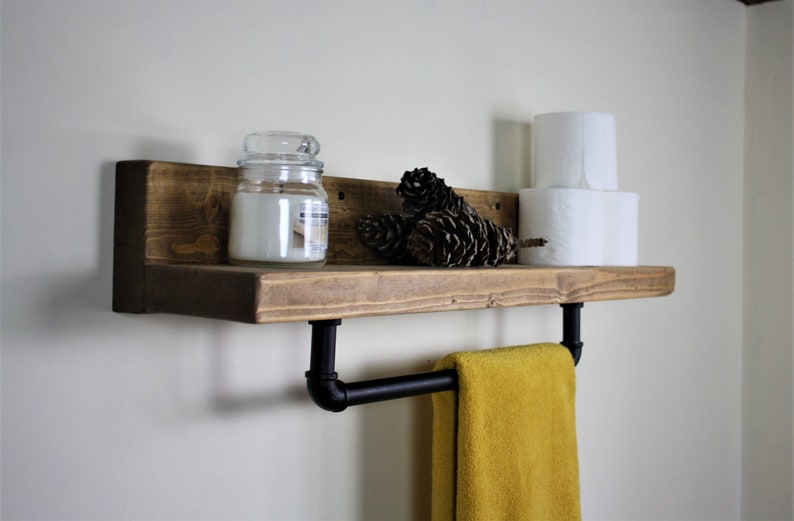 Pu&ograve; includere: Uno scaffale in legno rustico con una barra porta asciugamani in metallo nero attaccata. Lo scaffale &egrave; decorato con un barattolo di vetro per candele, pigne e due rotoli di carta igienica.