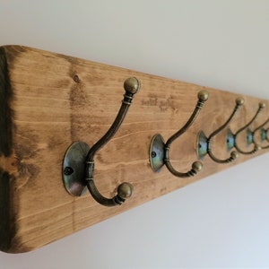 May include: A wooden coat rack with eight antique brass hooks. The rack is stained a dark brown color.