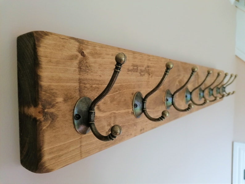 May include: A wooden coat rack with eight antique brass hooks. The rack is stained a dark brown color.