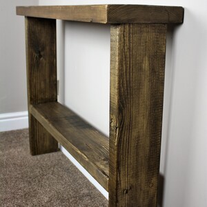 May include: A rustic wooden console table with a dark brown stain. The table has a single shelf and is made of reclaimed wood.