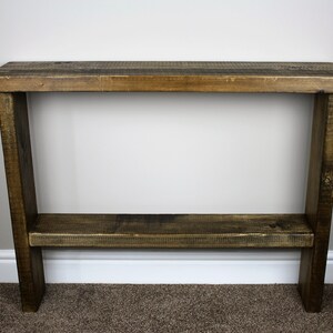 May include: A rustic wooden console table with a dark brown stain. The table has a single shelf and is made of reclaimed wood.