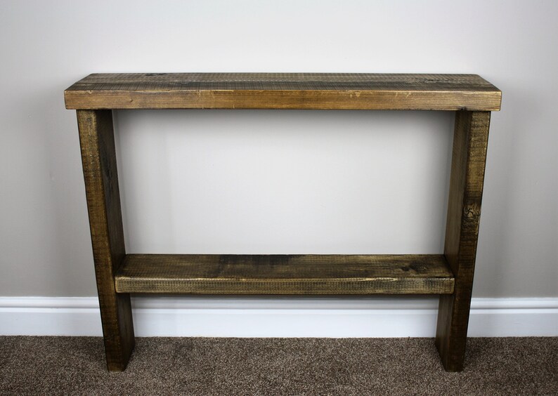 May include: A rustic wooden console table with a dark brown stain. The table has a single shelf and is made of reclaimed wood.