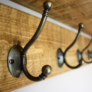 Peut inclure: Une &eacute;tag&egrave;re en bois avec cinq crochets en laiton antique. Les crochets sont fix&eacute;s &agrave; l'&eacute;tag&egrave;re avec des plaques rondes en m&eacute;tal. L'&eacute;tag&egrave;re est en bois de r&eacute;cup&eacute;ration et a une finition rustique.