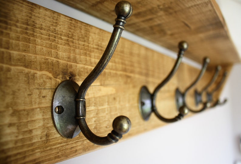 Peut inclure: Une &eacute;tag&egrave;re en bois avec cinq crochets en laiton antique. Les crochets sont fix&eacute;s &agrave; l'&eacute;tag&egrave;re avec des plaques rondes en m&eacute;tal. L'&eacute;tag&egrave;re est en bois de r&eacute;cup&eacute;ration et a une finition rustique.