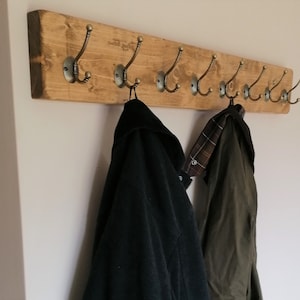 May include: A rustic wooden coat rack with multiple hooks, featuring a natural wood finish and antique brass hooks. Two coats are hanging on the rack, one black and one green.