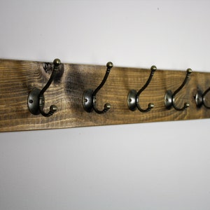 Puede incluir: Un perchero de madera r&uacute;stico con cinco ganchos de lat&oacute;n antiguo. El perchero est&aacute; hecho de madera marr&oacute;n oscura con un acabado natural.