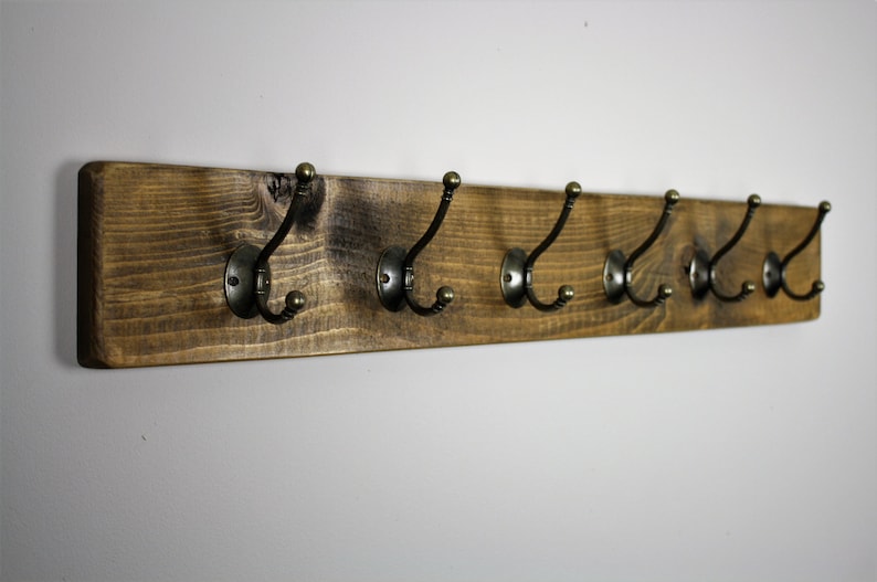 Puede incluir: Un perchero de madera r&uacute;stico con cinco ganchos de lat&oacute;n antiguo. El perchero est&aacute; hecho de madera marr&oacute;n oscura con un acabado natural.