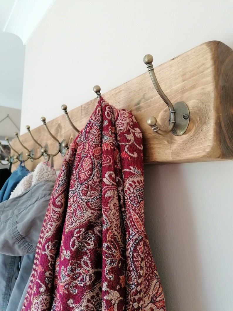May include: A wooden coat rack with multiple hooks, featuring a rustic finish. A red and gold patterned scarf hangs on one of the hooks.