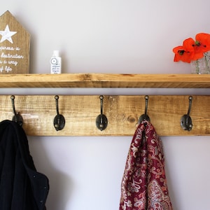 Peut inclure: Une &eacute;tag&egrave;re en bois avec cinq crochets, une petite pancarte en bois avec le texte "Le bonheur n'est pas une destination, c'est un mode de vie", et une petite bouteille de d&eacute;sinfectant pour les mains. Il y a aussi des fleurs rouges dans un bocal en verre sur l'&eacute;tag&egrave;re.
